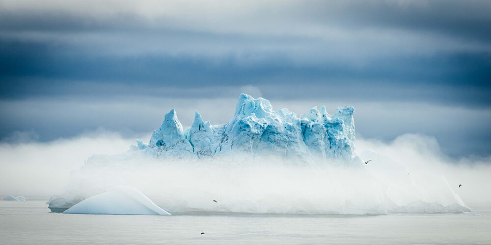 An iceberg emerges from a blanket of fog