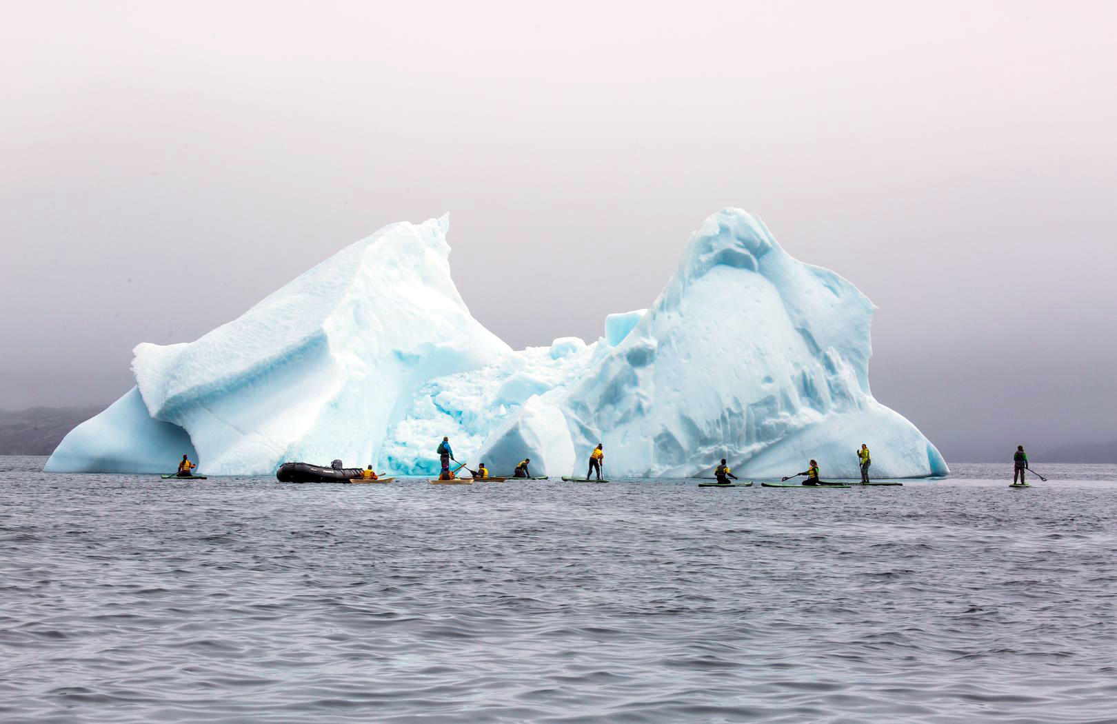 Expedition participants kayak and paddle board around an ice berg in the Labrador Sea